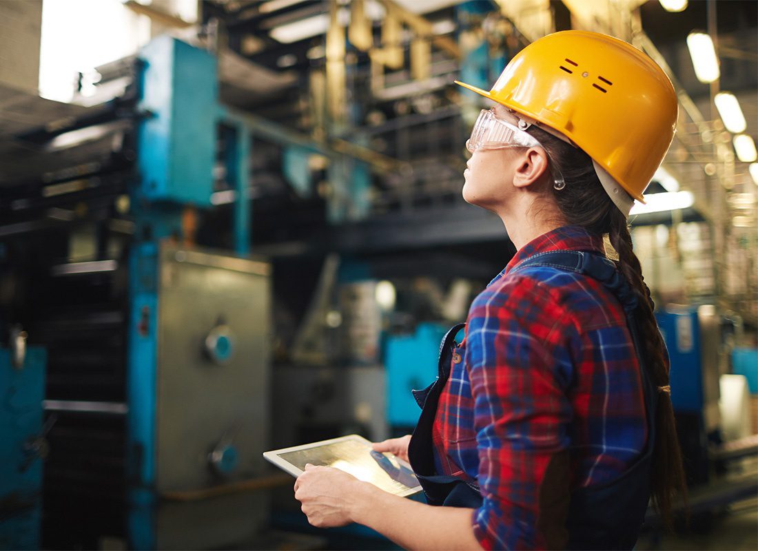 Read Our Reviews - Portrait of a Woman Working in a Manufacturing Facility Holding a Tablet in Her Hands While Looking at the Manufacturing Equipment